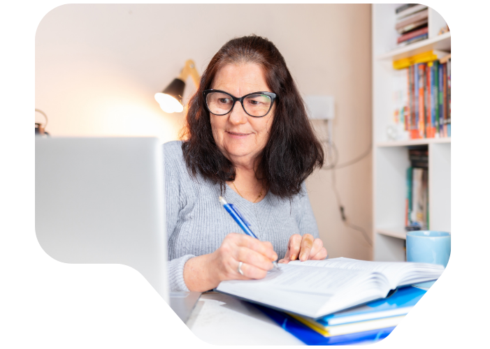 image of women sat at a desk, writing notes from her laptop into a notebook